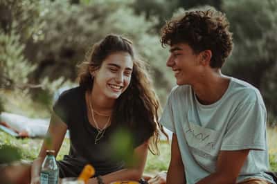 Una felice coppia di adolescenti si gode un picnic in un parco soleggiato, circondata da alberi verdi e lussureggianti.